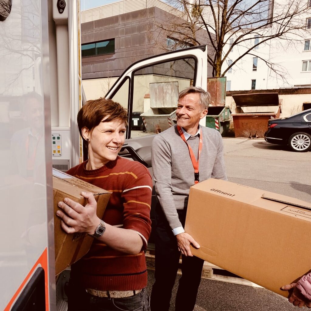 Barbara Likus lädt gemeinsam mit Klinikchef Axel Fischer Kisten in ein Rettungsauto.